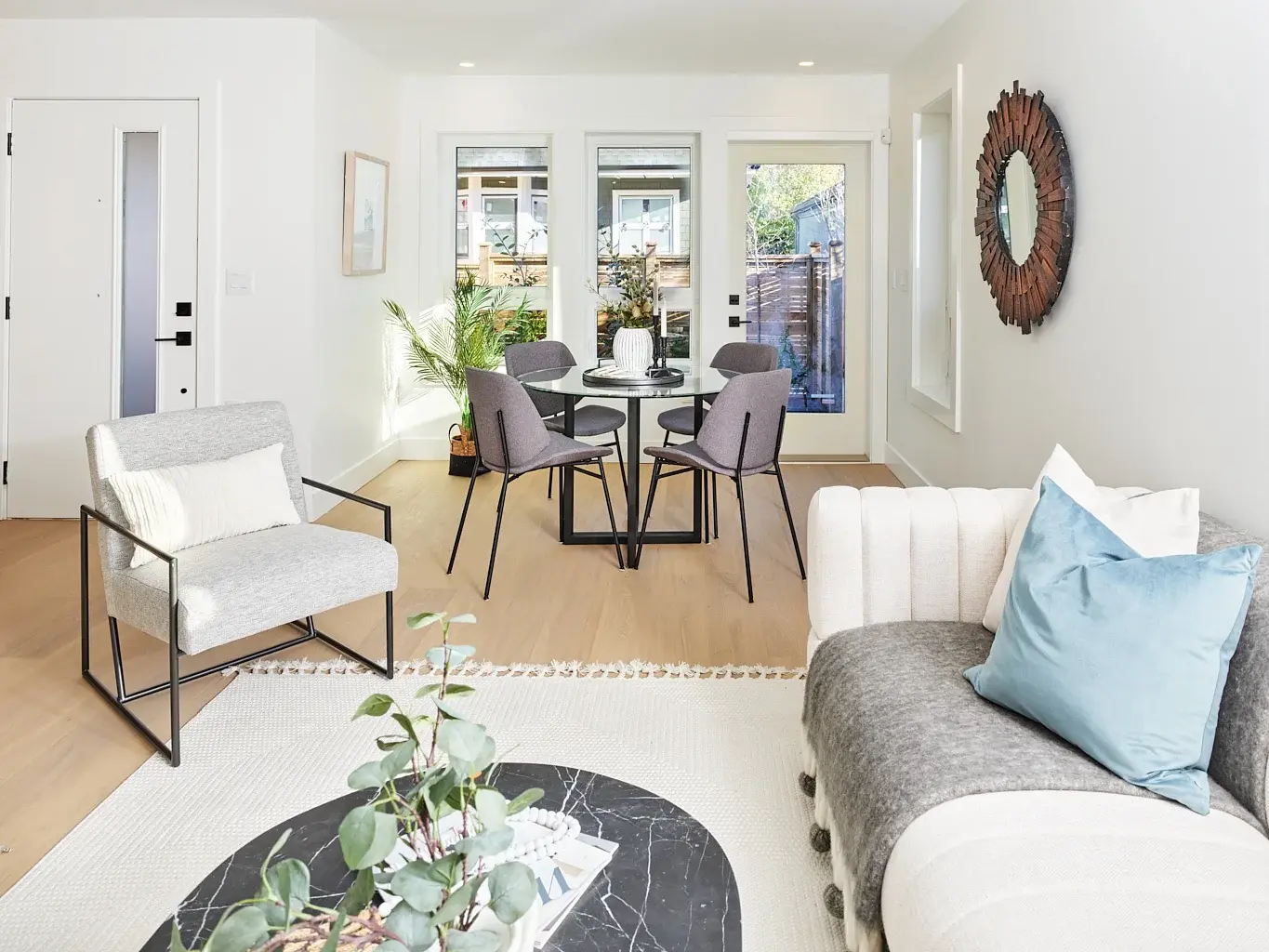 Vancouver living and dining area with round glass table, gray accent chairs, and sunburst mirror
