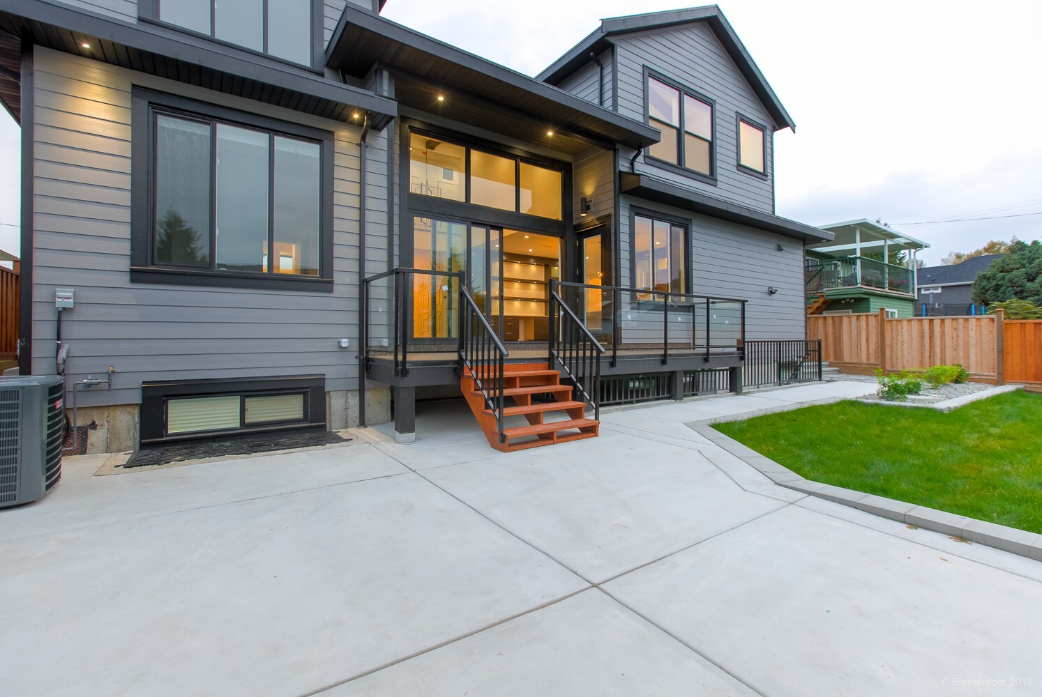Vancouver modern gray home backyard with covered deck, glass railings, and wood steps