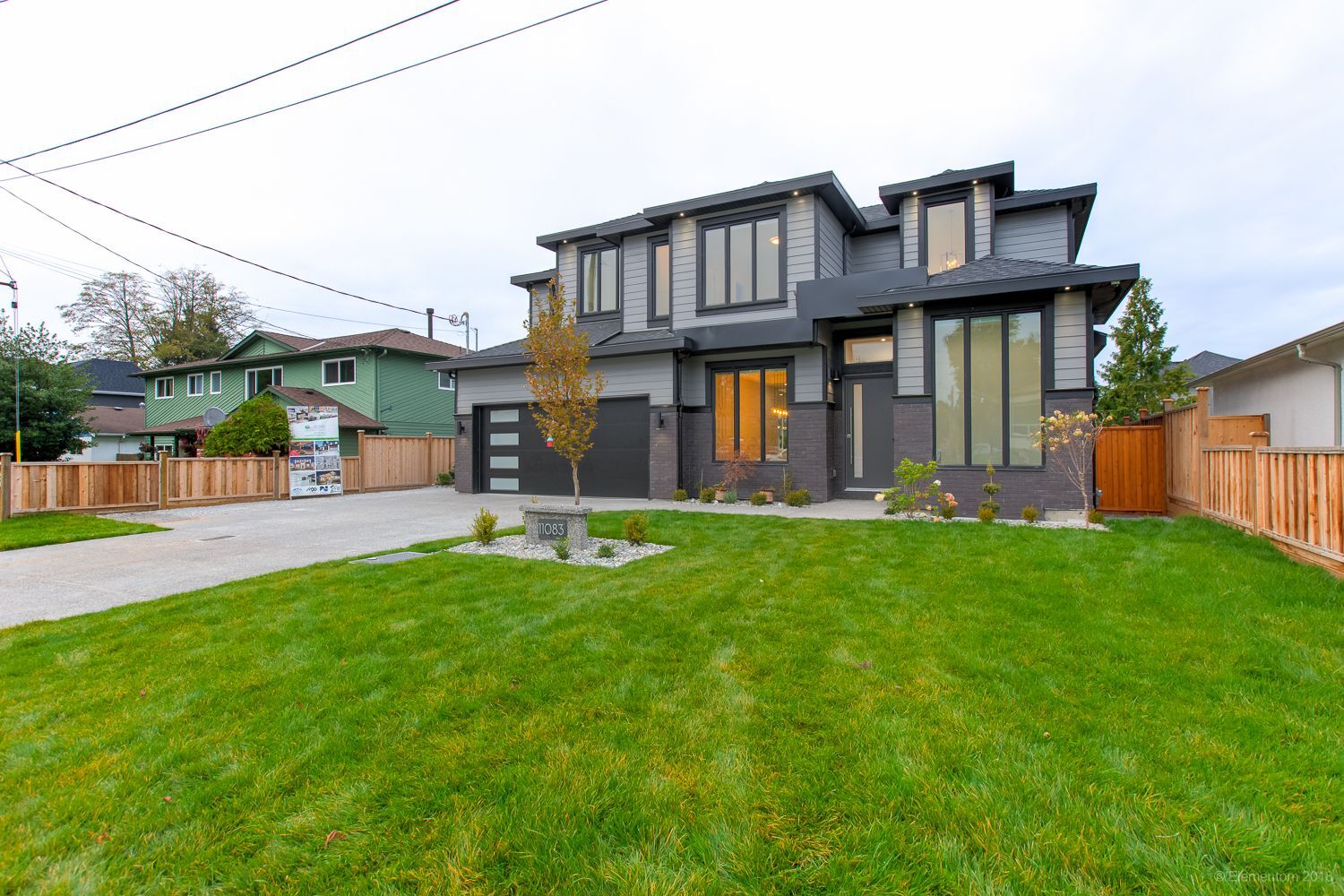 Vancouver two story home exterior with dark siding, brick accents, and illuminated entryway at dusk