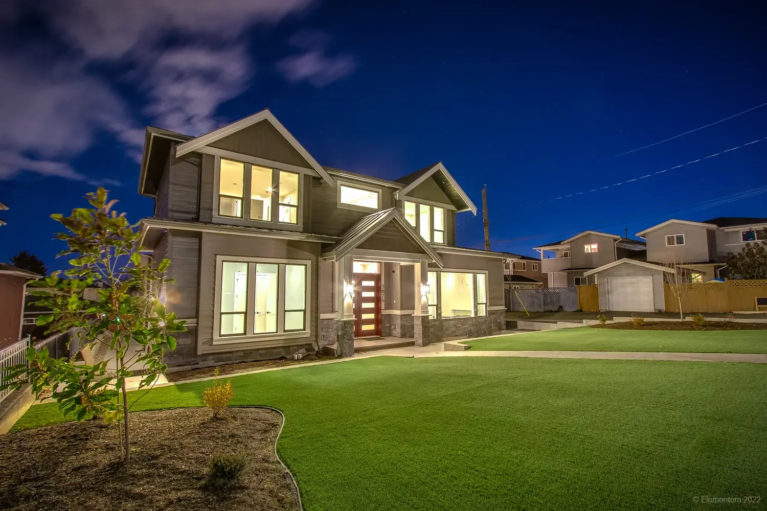 Vancouver two story home exterior with red front door, gabled roofline, and manicured lawn at night